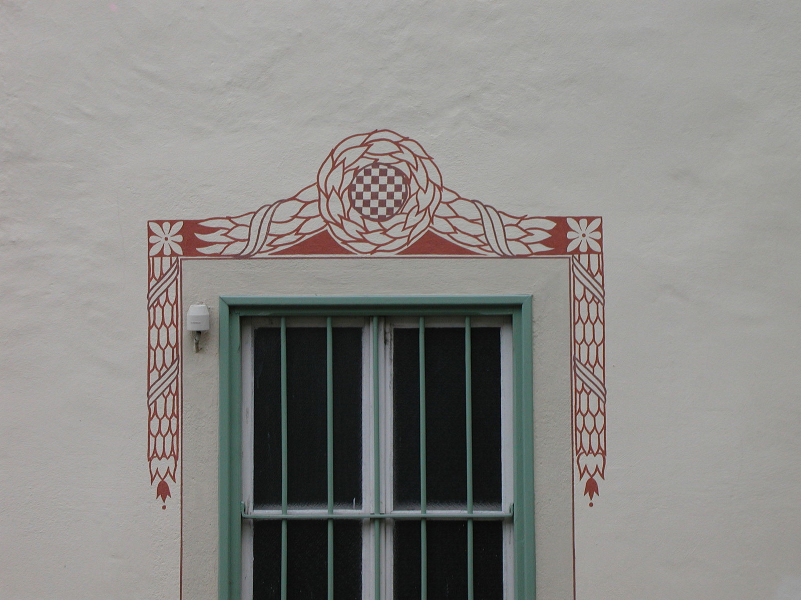 Restaurierte Sgraffito-Ornamentik über einem Fenster mit grünen Läden